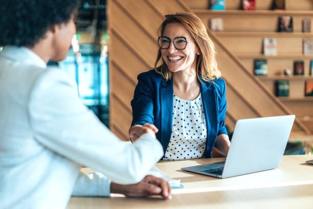 istockphoto-1460907602-612×612 Business people shaking hands in the office. Group of business persons in business meeting. Two entrepreneurs on meeting in board room. Corporate business team on meeting in modern office. Female manager discussing new project with her colleagues. Company owner on a meeting with her employee in her office.